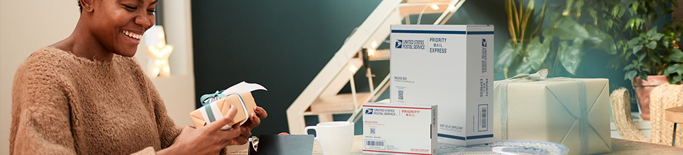 A woman prepares to pack and ship a holiday gift in a Priority Mail box.